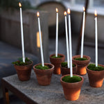 Smala vita ljus i små krukor på ett bord