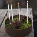 Smala stearinljus i mossa i en järnkruka